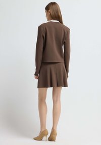 Brown sweater with a round collar, paired with a matching pleated skirt. Worn with beige open-toe heels featuring a woven design.