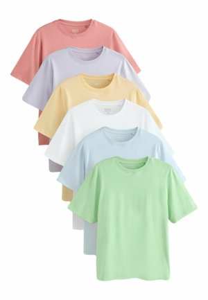 Młody mężczyzna z krótkimi włosami, ubrany w jasnoniebieski t-shirt z krótkim rękawem i niebieskie dżinsy, stojący na tle jednolitego jasnego tła.