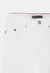 Weiße Denim-Jeans mit einer Vordertasche, die ein kleines Logo-Detail aufweist, einem Metallknopfverschluss und sichtbaren Nähakzenten.