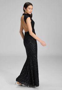 Musta, paljeteilla koristeltu iltapuku, jossa on muotoiltu pusero, hihattomat cap-hihat ja avonainen selkä. Leveä hameosa ulottuu lattiaan, mikä korostaa sulavalinjaista siluettia.