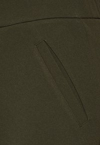 Olivgrüner Stoff mit einer glatten Textur; verfügt über eine horizontale Naht über einer Seitentasche mit rechteckiger Öffnung.