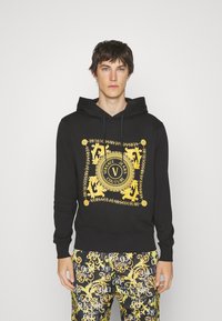 Felpa nera con cappuccio con un design stampato dorato che presenta motivi ornati e dettagli del logo. Tessuto morbido, tasca a marsupio e cappuccio con coulisse.