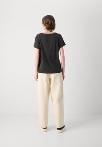 Maglietta nera a maniche corte con scollo rotondo, abbinata a pantaloni larghi color crema, indossati con scarpe di colore avorio. Design semplice.