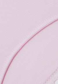 Primo piano di tessuto rosa chiaro con cuciture sottili e bordo a cucitura curva su uno sfondo uniforme.