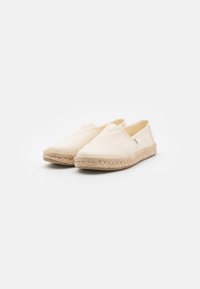 Espadrilles beige con parte superior de lona, suelas de yute trenzado y un diseño minimalista. Incluye acentos laterales elásticos para una fácil puesta.