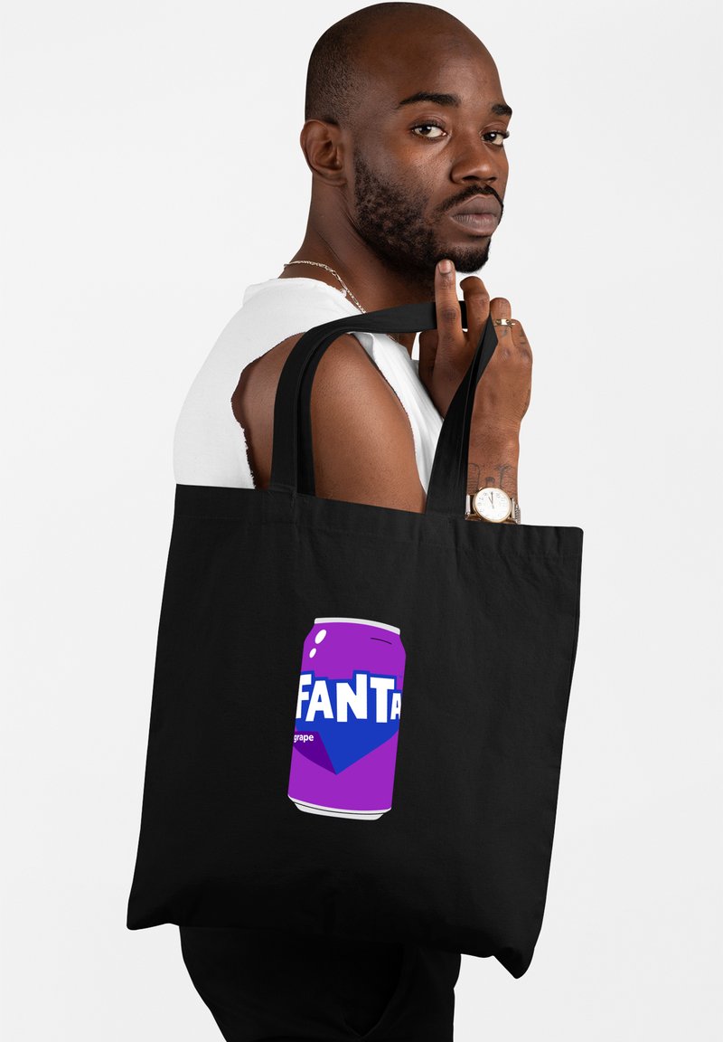 Zwarte tote bag met een paarse afbeelding van een Fanta druivensoda blikje. Het ontwerp bevat vetgedrukte witte letters op een gladde textuur.