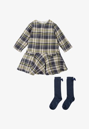 Vestido de cuadros en azul marino, verde y blanco con falda acampanada, dos bolsillos y mangas largas, combinado con calcetas hasta la rodilla en azul marino con lazos.