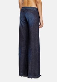 Pantalons en denim large couleur indigo foncé avec une taille élastique et des détails texturés subtils, présentant une finition propre à l'ourlet.