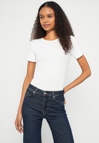 T-shirt blanc à manches courtes et coupe ajustée, associée à un jean denim bleu foncé taille haute. Texture lisse avec un col rond classique.