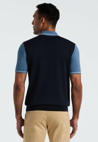 Mariene mouwloze polo met lichtblauwe korte mouwen, met een effen ontwerp en geribbelde ronde hals. Draag op khaki shorts, wat een ontspannen pasvorm laat zien.