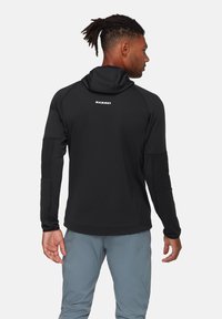 Czarna bluza z kapturem, z płaskimi szwami, elastycznymi mankietami i logo Mammut z tyłu. Posiada dopasowany krój oraz miękki, elastyczny materiał.