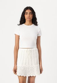Camiseta blanca corta combinada con una falda de punto crema texturizada, con cintura ajustable y detalle de dobladillo ondulado.