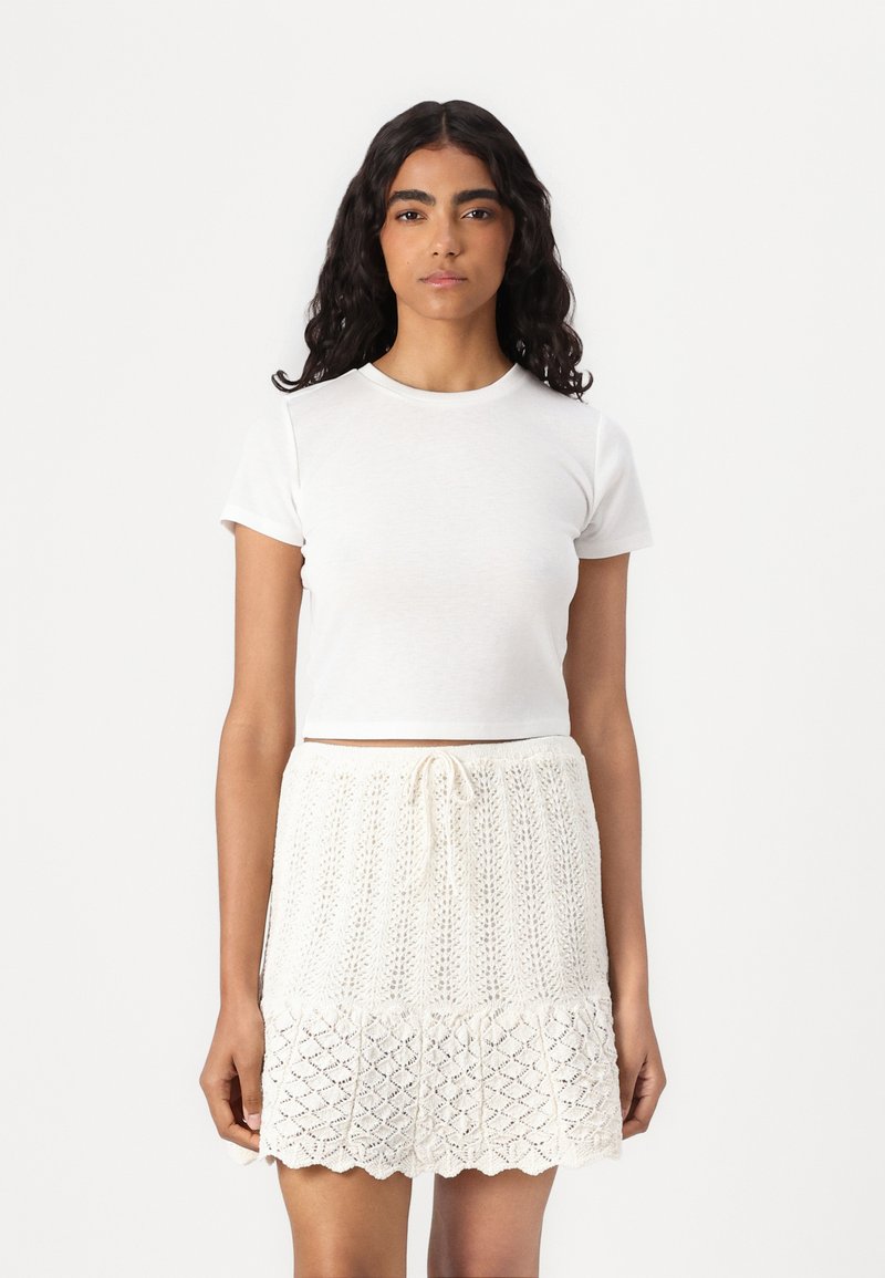 Camiseta blanca corta combinada con una falda de punto crema texturizada, con cintura ajustable y detalle de dobladillo ondulado.