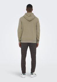 Hooded sweatshirt in light olive green, cotton blend fabric; paired with dark patterned trousers and white athletic shoes with green accents.