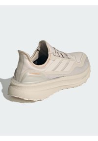 Light beige running shoe with a textured upper, three white stripes, and a cushioned sole. Features reinforced stitching and "ULTRABOOST" branding.