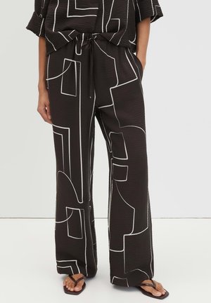 Zwarte broek met wijde pijpen en witte abstracte geometrische lijnen, gecombineerd met een bijpassende top, gedragen met zwarte sandalen met vierkante neus.