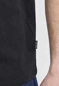 Svart bomulls T-skjorte med sideseam-etikett. Har en standard passform og myk tekstur, med synlige sømmer langs kanten.