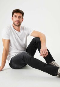Camiseta blanca de algodón para hombre combinada con Jeans ajustados negros. El conjunto presenta un diseño casual y está complementado con zapatillas grises.