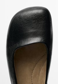 Zwarte leren platte schoen met een afgeronde vierkante neus en een beige binnenzool met gestikte details.