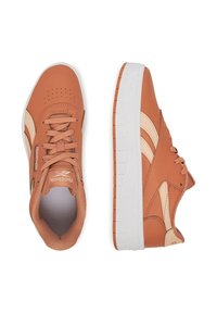 Pár ružovo-hnedých tenisiek Reebok s bielymi podrážkami a béžovými bočnými pruhmi, z ktorých jeden zobrazuje pohľad zhora a druhý bočný pohľad.