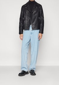 Osoba w czarnej skórzanej kurtce nosząca czarny golf, połączona z jasnoniebieskimi spodniami o szerokich nogawkach i czarnymi, masywnymi butami.