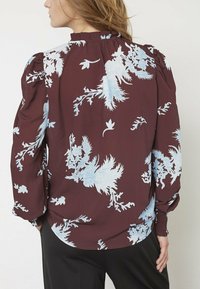 Bordeaux-blomsterbluse med blå blomsterprint; har puffede ærmer, rynket halsudskæring og elastiske manchetter; lavet af letvægtsstof.