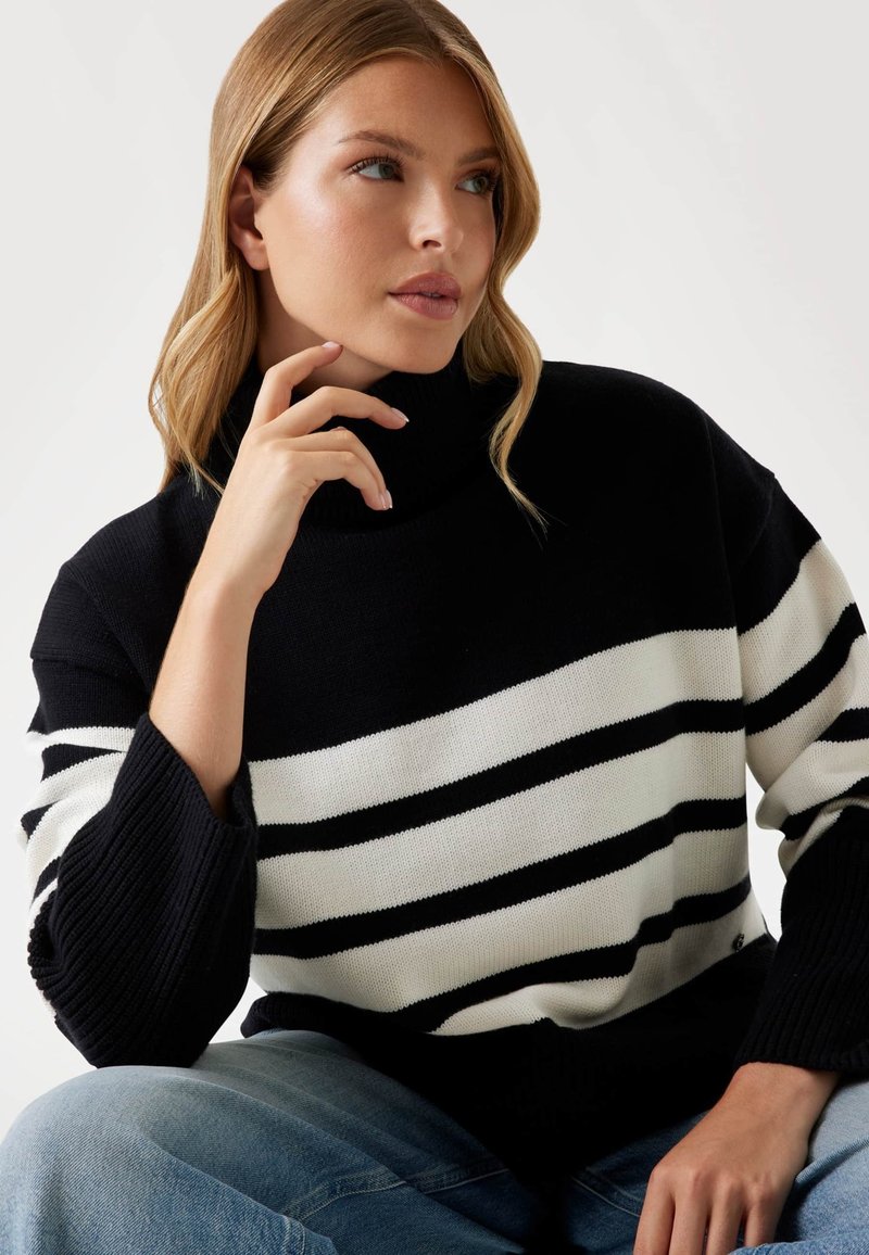 Maglione a collo alto a righe bianco e nere con polsini a costine, caratterizzato da una vestibilità comoda e una texture lavorata a maglia. Abbinato a jeans in denim azzurro chiaro.