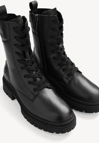 Black leather lace-up boots with a zipper on one side, a thick sole, and a rounded toe. Textured finish and sturdy laces.