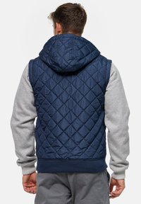 Chaleco acolchado azul marino con capucha, mangas grises, dobladillo acanalado y un patrón de diamantes. Material ligero, diseñado para uso casual.