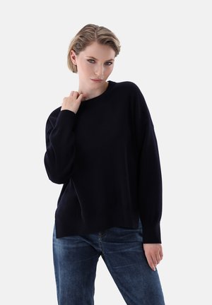 Navy blue sweater in soft fabric, featuring a crew neck, long sleeves, and a relaxed fit with a slightly longer back hem, paired with jeans.