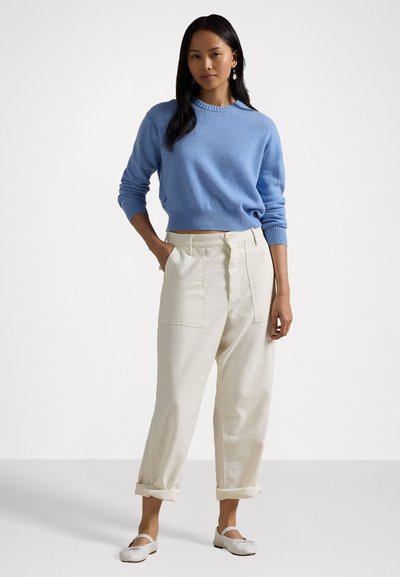 Pulover tricotat de culoare bleu deschis, cu guler cu nervuri, asortat cu pantaloni largi de culoare crem, cu buzunare laterale și margini răsfrânte. Pantofi albaștri tip slip-on.