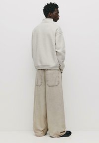 Hanorac bej cu guler înalt, asortat cu pantaloni de blugi bej, largi, cu două buzunare la spate. Design simplu, cu o croială lejeră.