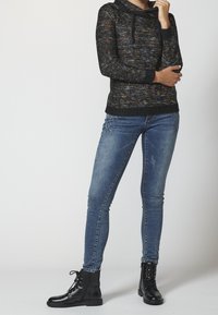 Černý pletený svetr s vícebarevnými tečkami, rolákem a stahovací šňůrkou. Kombinován s modrými úzkými džíny a černými šněrovacími botami.