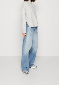 Ljusgrå långärmad topp med hög halskrage, kombinerad med vida ljusblå denimjeans. Sneakers med silverdetaljer fulländar looken.