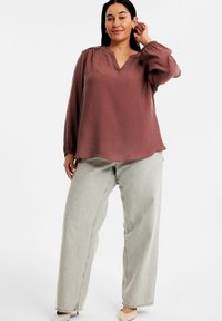 Bordeauxblus med långa puffärmar och V-ringning, kombinerad med ljusgrå vida jeans och ljusa klackar. Slät tygtextur.