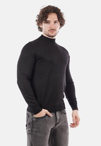 Maglione a girocollo nero a maglia con maniche lunghe, polsini e orlo a coste. Realizzato in tessuto morbido, forma aderente, indossato sopra jeans grigio scuro.