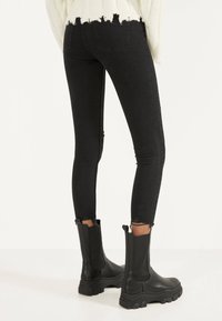 Jeans skinny negros con bajos desgastados, combinados con botines negros gruesos. Los jeans presentan un diseño ajustado y bolsillos traseros sutiles.