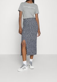 Harmaa puuvillainen t-paita, jossa "TOMMY HILFIGER" -logo, yhdistetty polvipituiseen tummansiniseen hameeseen, jossa kukkakuvio ja sivuhalkio. Valkoiset tennarit.