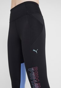 Zwarte sportleggingen met een hoge tailleband, zijpaneel in lichtblauw en een multikleurig "PUMA"-logo dat langs het been is gedrukt.