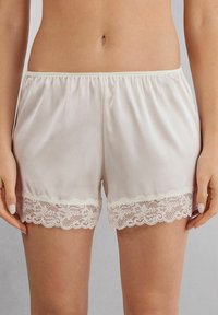 Satin shorts in gebroken wit met een elastische tailleband. De zoom heeft ingewikkelde kantdetails, wat textuur en contrast toevoegt.