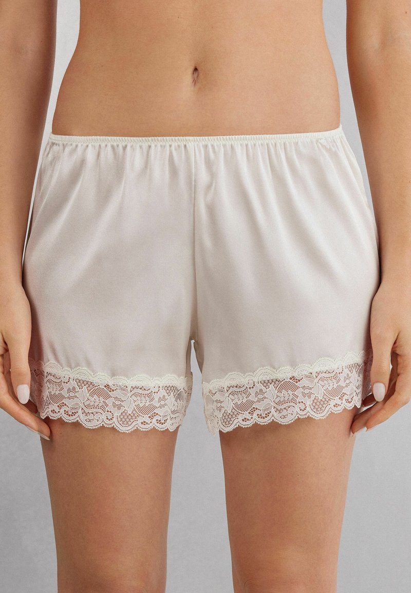 Satin shorts in gebroken wit met een elastische tailleband. De zoom heeft ingewikkelde kantdetails, wat textuur en contrast toevoegt.