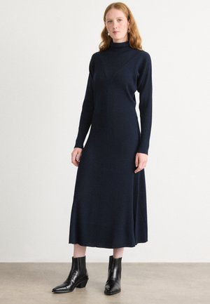 Navy ribbed knit dress with a high neckline, long sleeves, and a flared hem; paired with black ankle boots. Smooth texture and tailored fit.
