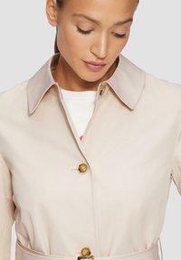 Beige trenchcoat met een lichtgrijze kraag, voorzien van gouden knopen en een belted taille. Gladde textuur, modern ontwerp.