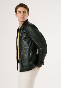 Chaqueta de cuero negra con cremallera en el frente, dos bolsillos frontales y corte recto. Textura suave, cuello clásico y diseño minimalista.