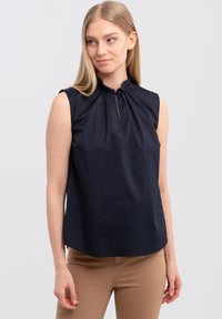 Navyblauwe mouwloze blouse met een geraffineerde halslijn en een klein keyhole-detail, gemaakt van gladde stof met een ontspannen pasvorm.
