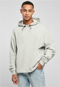 Sudadera gris clara con capucha ajustable, corte oversize, puños acanalados y textura suave. Llevada con unos vaqueros de denim azul claro.