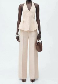 Béžový peplum top s výstřihem do V a knoflíky, kombinovaný s vysokými širokými kalhotami. Ruce držící malou hnědou kabelku.