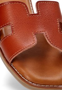 Sandalia de cuero marrón tipo slide con punta abierta. Presenta un destacado diseño con cortes, costuras blancas y una suela suave y duradera.