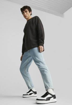 Maglietta nera a maniche lunghe, jeans in denim blu chiaro e sneakers bianco e nere. Design semplice, vestibilità rilassata, tessuto testurizzato in colori neutri.