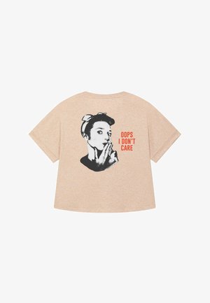 Losse, perzikkleurige t-shirt gemaakt van zachte stof met een zwarte afbeelding van een vrouw met een bandana en de tekst "OOPS I DON’T CARE."